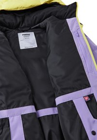Gelber und lila Innenfutter der Jacke mit einem glatten schwarzen Futter. Merkmale sind ein eingenähter Aufnäher und eine Seitentasche mit Reißverschluss.