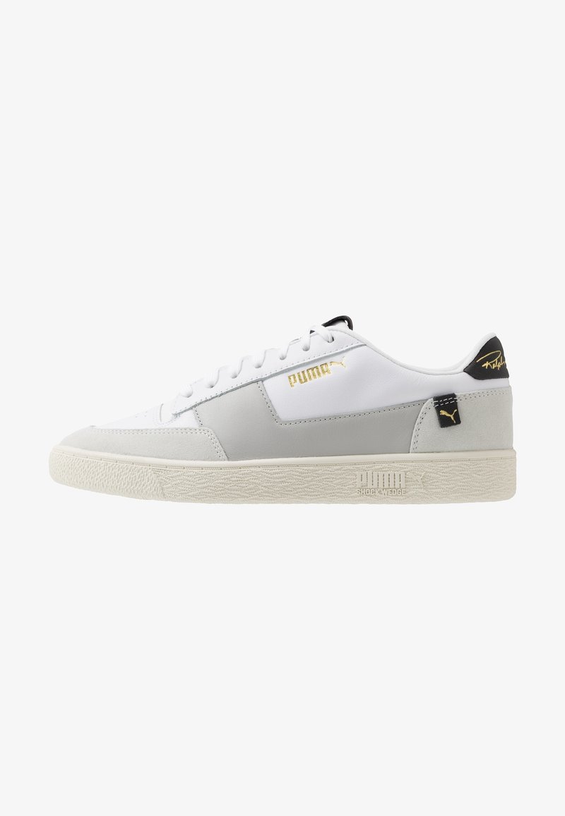 Baskets basses Puma blanches et grises avec logo doré, languette noire au talon et semelle crème texturée avec marquage Puma Shock Wedge.
