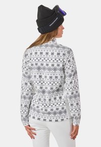 Biały polarowy sweter z czarnym geometrycznym wzorem. Posiada długie rękawy, wysoki kołnierz i luźny krój. W komplecie z czarną czapką beanie i okularami.