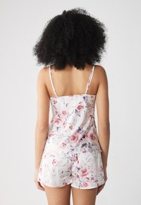 Set de pijama cu model floral, realizat dintr-un material ușor. Topul are bretele subțiri, iar pantaloni scurți sunt largi și prezintă un design floral similar.