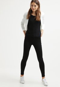 Svart strikkegenser, hvit kort blazer, svarte skinny jeans og hvite sneakers. Enkelt design med glatt tekstur og tettsittende form.