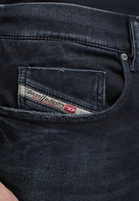 Κοντινή λήψη μαύρου τζιν με έμφαση στην μικρή μπροστινή τσέπη που διαθέτει υφασμάτινη ετικέτα Diesel Industry.