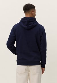 Tmavomodrá mikina s kapucňou vyrobená z mäkkého materiálu, vybavená veľkou prednou kapsou a kapucňou so šnúrkou. Hladká štruktúra s rebrovanými manžetami.