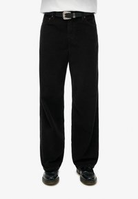 Zwarte corduroy broek met een wijd uitlopende pasvorm, voorzien van een zilveren ceintuurgesp en oranje stiksels. Gestructureerd oppervlak met verticale rimpels.