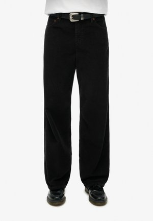 Zwarte corduroy broek met een wijd uitlopende pasvorm, voorzien van een zilveren ceintuurgesp en oranje stiksels. Gestructureerd oppervlak met verticale rimpels.