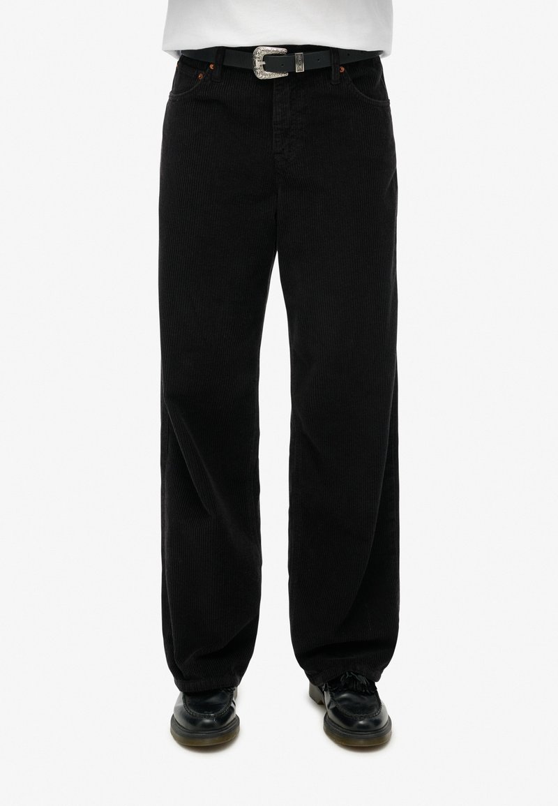 Zwarte corduroy broek met een wijd uitlopende pasvorm, voorzien van een zilveren ceintuurgesp en oranje stiksels. Gestructureerd oppervlak met verticale rimpels.