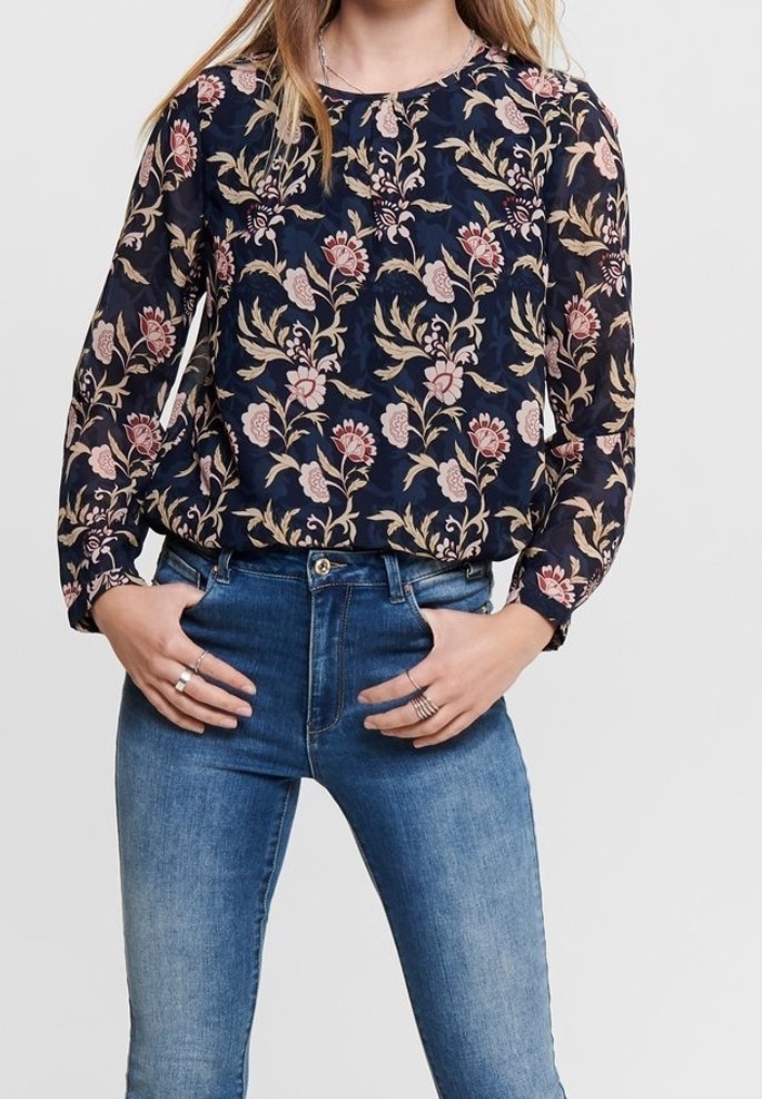 Blusa a maniche lunghe blu navy con motivo floreale in rosa e beige. Tessuto leggero, scollatura rotonda, vestibilità comoda, abbinata a jeans azzurri chiari.
