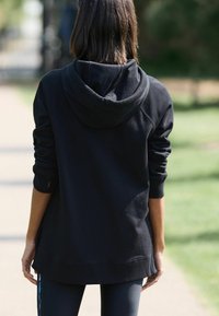 Felpa nera con cappuccio, maniche lunghe, texture morbida e vestibilità rilassata. Cuciture visibili e dettaglio dell'orlo curvo sul retro.