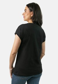 Camiseta negra de manga corta con cuello redondo, corte holgado y textura suave. La vista trasera muestra un acabado liso y un diseño relajado.