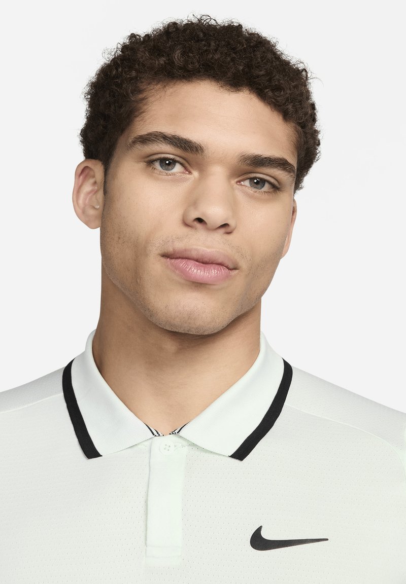 Camisa polo verde claro con detalles en negro, que presenta un cuello de dos botones, tejido texturizado y un destacado logo negro de Nike en el pecho.