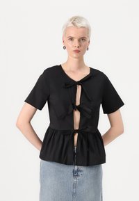 Svart kortermet topp med peplum-design, med knyte-lukking foran og utskårne detaljer, laget av glatt stoff.