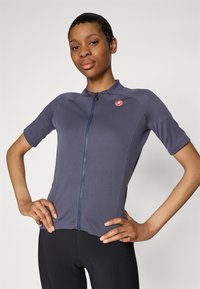 Maillot de cyclisme à manches courtes en tissu bleu foncé, présentant une fermeture éclair à l'avant et un logo discret sur la poitrine. Design lisse et ajusté.
