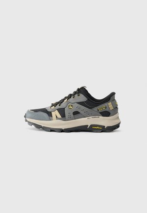 Black and gray all-terrain athletic shoe with beige accents, lace-up design, and Goodyear sole branding on a white background.
