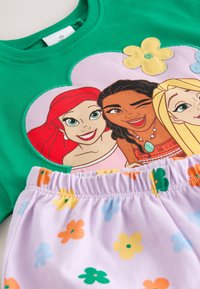 Camisa verde con estampados de dibujos animados de tres chicas sonrientes y pantalones cortos morados con patrones de flores multicolores y cintura elástica.