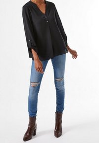 Blusa negra de manga larga con escote en V y dos botones en la parte delantera, combinada con jeans claros rotos y botas de tobillo marrones con tacón.