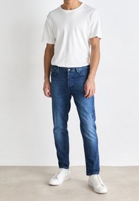 Biała koszulka z krótkim rękawem, niebieskie dżinsy z denimu oraz białe trampki. Dżinsy mają prosty krój i klasyczny fason z pięcioma kieszeniami.