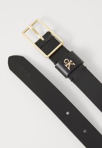Zwarte leren riem met een rechthoekige goudkleurige gesp, gegraveerd 'CK' logo op de band en vijf gaten voor verstelbare maat.