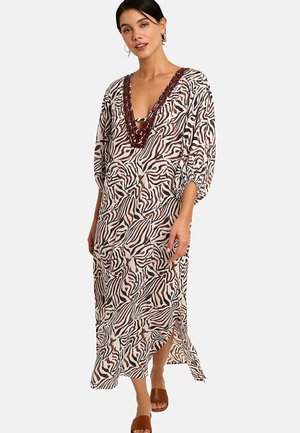 Femme portant une longue robe à imprimé zèbre avec des manches ballon, un décolleté en V profond bordé de brun, et des sandales marron à enfiler.