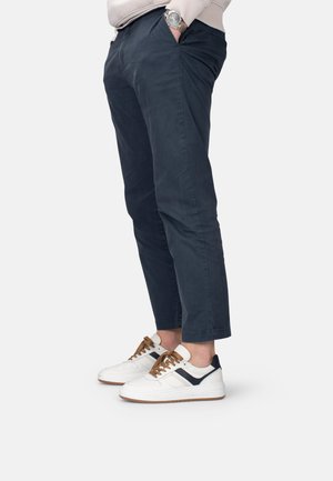 Chinos de algodón en color navy con bolsillos laterales, con un diseño ajustado. Combinados con zapatillas blancas con detalles en navy y cordones marrones.