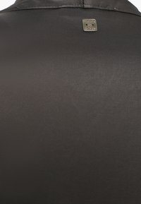 Tessuto di satin nero con una superficie liscia, presenta un'etichetta metallica con logo impresso sul retro del colletto. Design semplice ed elegante.