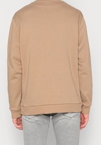 Felpa beige con collo a giro e polsini a coste. Texture liscia, design minimale, cuciture visibili e assenza di elementi grafici.