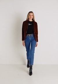 Brun fløjl blazer over en sort t-shirt, parret med blå jeans og sorte ankelstøvler. Enkel design med en tætsiddende silhuet.