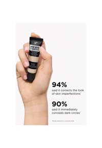 Main tenant un tube de correcteur IT Bye Bye Under Eye avec des échantillons sur le poignet et un texte indiquant 94 % de correction des imperfections de la peau, 90 % de dissimulation des cernes.