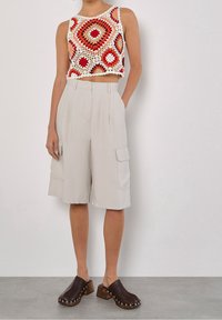 Gebreide crop top in rood, oranje en witte patronen; beige cargoshorts met plooien en zijzakken; donkerbruine klompen met houten hakken.