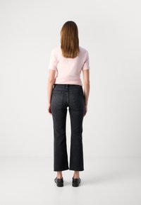 Høyt liv svart denim flared jeans med rå kant, sammen med en lyserosa tettsittende kortermet topp, sett fra baksiden.