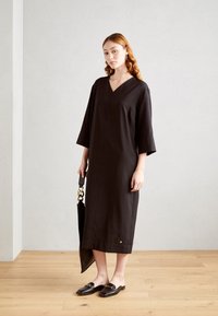 Robe en lin noire avec un col en V, des manches trois-quarts, une coupe droite et une petite poche. Associée à des chaussures noires à enfiler et un sac.