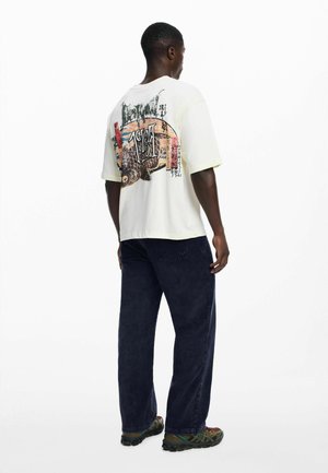 White oversized t-shirt with colorful graphic print on the back, paired with navy blue relaxed-fit pants and multicolored athletic shoes.