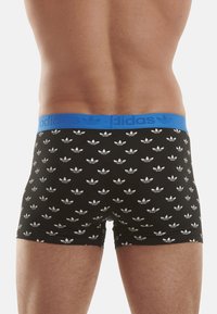 Caleçons boxer avec une ceinture bleue et un motif répétitif de trèfle Adidas blanc sur fond noir. Fabriqués en tissu extensible.