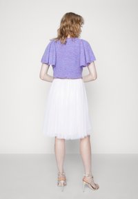 Paarse gebreide top met pofmouwen, gecombineerd met een witte tule rok. Schoeisel bestaat uit beige hakken met enkelbandjes.