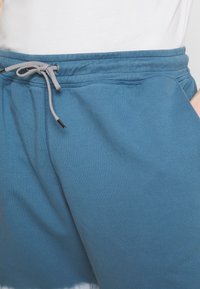 Modré bavlněné tepláky s elastickým pasem, šňůrkou v šedé barvě, bočními kapsami a hladkým povrchem.
