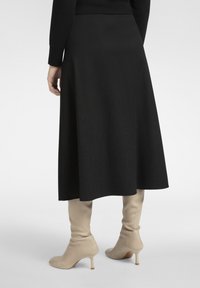 Schwarzer A-Linien-Midirock mit glatter Textur, kombiniert mit kniehohen beigen Stiefeln mit Absatz. Klare Silhouette ohne sichtbare Muster oder Verzierungen.