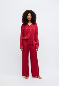 Set de pijamale din satin roșu cu modele geometrice, compus dintr-un top cu nasturi și mâneci lungi și pantaloni largi. Textură netedă, croială lejeră.