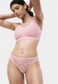 Růžová podprsenka s texturovanou látkou, krajkovým lemem a malou mašlí. K ní ladící růžové krajkové tanga s květinovým vzorem a vroubkovanými okraji.