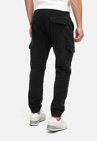 Black corduroy cargo pants with elastic cuffs, two rear flap pockets, and a relaxed fit. Paired with white and gray athletic shoes.