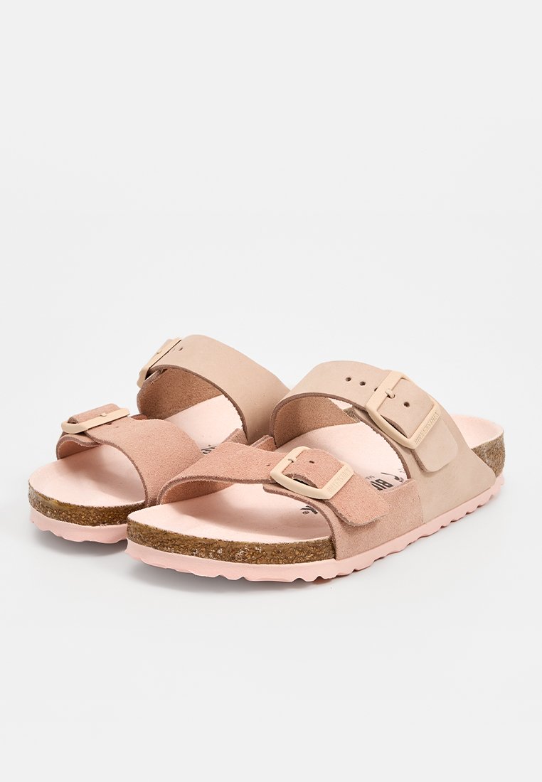 Ein Paar rosa und beige Wildledersandalen mit verstellbaren Schnallen, Korkfußbetten und strukturierten Gummisohlen auf einem weißen Hintergrund.