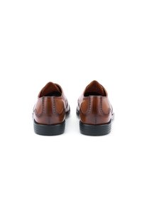 Chaussures en cuir marron avec une texture lisse, ornées de détails de brogue, et semelles en caoutchouc noir. Vue de l'arrière, mettant en évidence la forme.