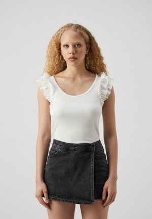 Hvit stripete tank topp med volanger på skuldrene, sammen med en mørk denim omslagskjørt med sidelukking med knapper og frontlommer.
