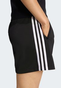 Pantaloncini sportivi neri in materiale sintetico, con tre strisce verticali bianche sul lato e una tasca laterale.