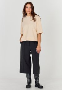 Beežikas ülepaistvast lühikeste varrukatega top, millele on lisatud kõrge vöökohaga mustad laiad püksid ja põlveni ulatuvad mustad saapad. Silmapaistev materjal, lõdvestunud istuvus.