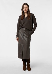 Brązowy sweter w serek w połączeniu z ciemnobrązową skórzaną spódnicą ołówkową do kolan, uzupełnioną brązowymi zamszowymi botkami do kolan.