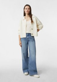 Biały, teksturowany kardigan z kołnierzykiem i drewnianymi guzikami, w połączeniu z jasnoniebieskimi szerokimi spodniami i kremowymi trampkami.