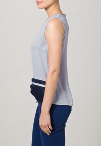 Ärmlös topp i ljusgrå satin med en marinblå framficka med horisontella vita ränder, slät textur och avslappnad passform.