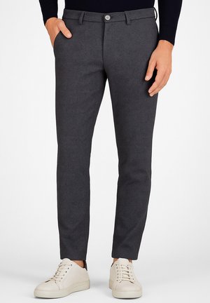 Pantalons gris ajustés avec une texture subtile, dotés de poches avant et d'une fermeture à bouton, associés à des baskets de couleur claire.