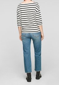 Pruhovaný top s lodním výstřihem a tříčtvrtečními rukávy v černé a bílé barvě, kombinovaný se světle modrými rovnými džíny a černými platformovými botami.