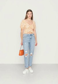 Top cropped amarelo com estampado floral de mangas curtas, jeans rasgados azuis claros, tênis brancos e uma pequena bolsa laranja. Tecido suave com um corte descontraído.
