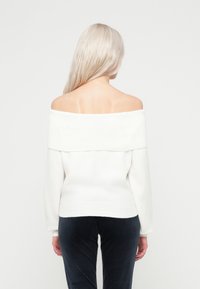 Λευκό πουλόβερ με ανοιχτούς ώμους, ριγωτή λαιμόκοψη, απαλό υλικό και εφαρμοστή γραμμή. Συνδυασμένο με σκούρους μπλε βελούδινους παντελόνες.